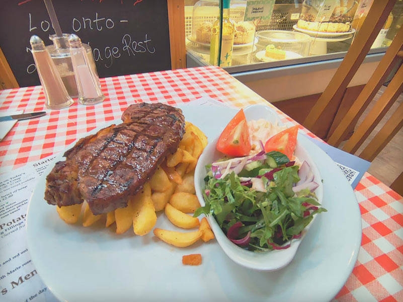 Steak and chips with a side salad in a red and white checkered tablecloth